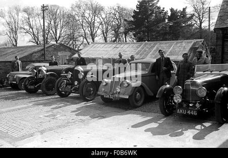 Un line-up de Bentley et Aston Martin voitures et leurs propriétaires à l'extérieur d'une maison dans le pays. Banque D'Images