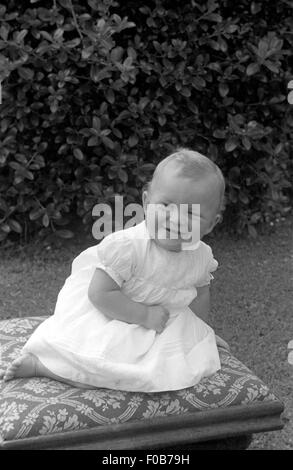 Un jeune bébé aux cheveux juste assis sur un tabouret rembourré en souriant. Banque D'Images