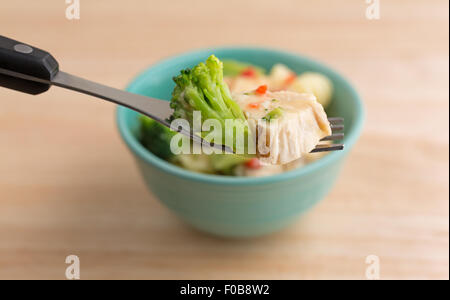 Fermer la vue d'une fourchette avec un morceau de brocoli et du poulet grillé dans une sauce à l'ail dans l'avant-plan Banque D'Images