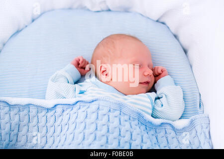 Bébé nouveau-né garçon au lit. Nouveau-né dort sous une couverture en tricot bleu. Les enfants dorment. La literie pour enfants. Banque D'Images