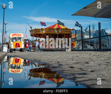 Carousel ride et forains vintage ice cream van sur le Barbican de Plymouth reflété dans une flaque d'eau après une douche de pluie. Banque D'Images