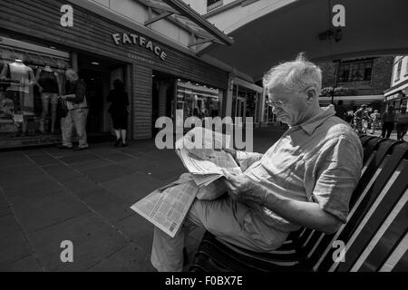 Homme lisant un journal assis sur un banc dans shopping centre Salisbury Wiltshire Banque D'Images