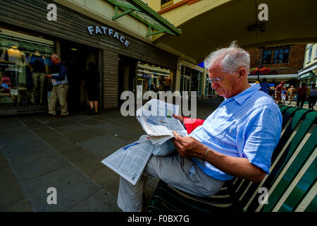 Homme lisant un journal assis sur un banc dans shopping centre Salisbury Wiltshire Banque D'Images