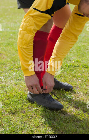 La section basse de l'homme attachant chaussures de football sur terrain Banque D'Images