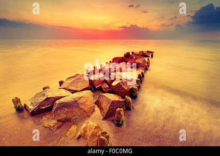 Magnifique coucher de soleil sur plage et jetée de rochers. Banque D'Images