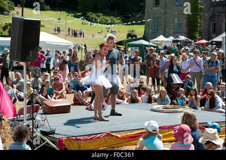 Famille regarder un acte acrobatique dans le soleil d'été par des stands de nourriture et de tentes au Port Eliot Cornwall Festival Banque D'Images