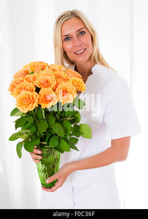 Infirmière blonde tenant un vase de roses et de sourires Banque D'Images