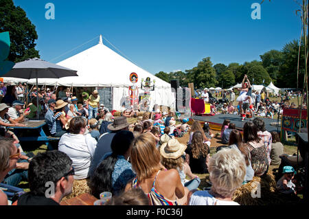 Famille regarder un acte acrobatique dans le soleil d'été par des stands de nourriture et de tentes au Port Eliot Cornwall Festival Banque D'Images