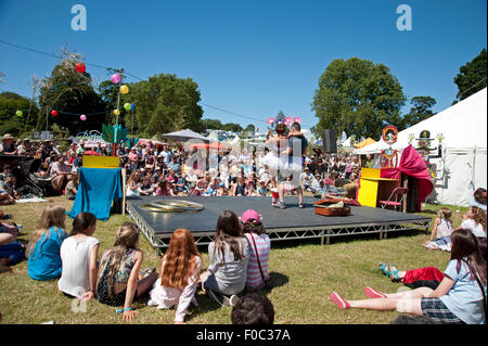 Famille regarder un acte acrobatique dans le soleil d'été par des stands de nourriture et de tentes au Port Eliot Cornwall Festival Banque D'Images