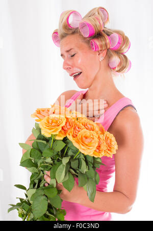 Femme blonde avec des bigoudis rose tient un bouquet de roses Banque D'Images