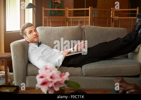 Portrait d'un homme portant des vêtements intelligents portant sur canapé using laptop Banque D'Images