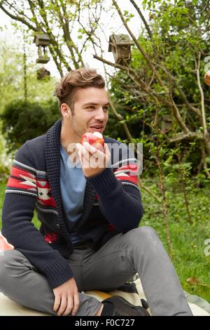 Portrait of smiling man sitting in garden de manger une pomme Banque D'Images