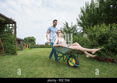 Man pushing wheelbarrow at girlfriend in backyard Banque D'Images