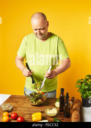 Salade fraîche ingrédients sur la table, homme d'âge moyen - salade mélange fond jaune Banque D'Images