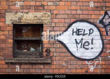 "Aidez-moi !' mots écrit en graffiti peint bulle à côté de la fenêtre sont montés à bord du bâtiment abandonné en brique rouge wal Banque D'Images