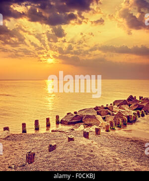 Coucher de soleil spectaculaire aux couleurs rétro sur plage et jetée de rochers. Banque D'Images