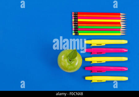Retour à l'école ou de bureau Fournitures composé d'une pomme verte, mettre en évidence des marqueurs et crayons de couleur sur fond bleu. Banque D'Images