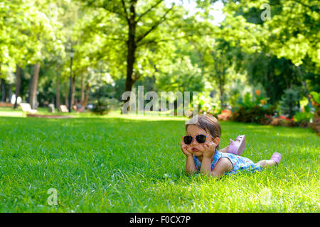 Cute little girl pose dans l'herbe sur un jour d'été ensoleillé Banque D'Images