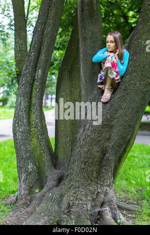 Petite fille mignonne assis sur un arbre. Banque D'Images