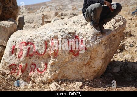 Ramallah, Cisjordanie, territoire palestinien. Août 13, 2015. Un palestinien se trouve sur le rocher de l'écriture graffiti écrit en hébreu dans la région d'Ein Samiya près de Kafr Malik village dans le nord de Ramallah, le 13 août, 2015. Un groupe de colons israéliens ont attaqué le village de Ein Samiya et jeté les matériaux inflammables sur une tente bédouine avant les résidents remarqué et attaqué les colons, ce qui les rend immédiatement fuir la région Crédit : Shadi Hatem/APA/Images/fil ZUMA Alamy Live News Banque D'Images