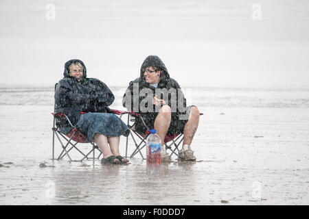 Deux personnes assis sur une plage dans un violent orage. Les deux rient comme la bourrasque soudaine s'infiltre entre eux. Ils sont typiquement français et de l'assis dehors. Banque D'Images