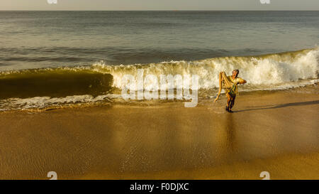 Pêcheur se fait surprendre par une grande vague puisqu'il s'apprête à enregistrer son petit filet de la plage de sable dans la mer d'Oman. Banque D'Images
