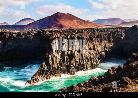 Los Hervideros littoral, à Lanzarote avec des vagues et le volcan Banque D'Images