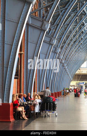 Voyageurs assis sous la charpente métallique de la gare St Pancras Londres Banque D'Images