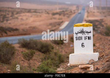 Sidi Ifini 6 kilomètres - distance panneau indicateur sur la route de Sidi Ifini avec la route dans l'arrière-plan, Maroc Banque D'Images