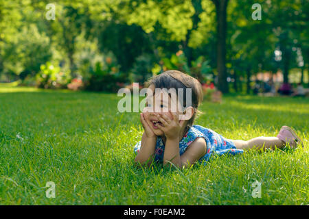 Cute little girl pose dans l'herbe sur un jour d'été ensoleillé Banque D'Images