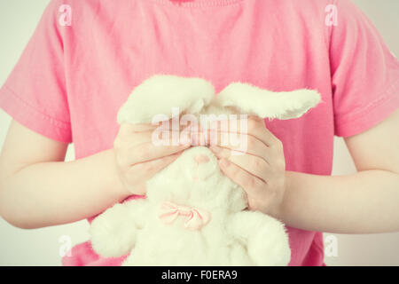 Little girl holding animal en peluche avec ses mains. Il est couvrant les yeux de la peluche lapin. Image conceptuelle de l'insécurité de la petite enfance, l'innocence et de la vulnérabilité. Banque D'Images