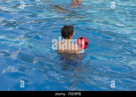 Jouer avec une boule rouge dans la piscine Banque D'Images