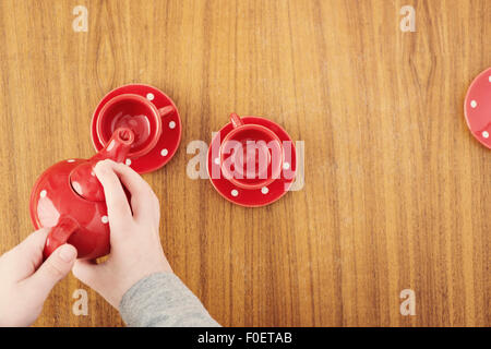 Petite fille qui sert de plateau pot à teaparty. Vue de dessus de tasses et les mains de l'enfant. L'image montre un adorable moment de jeux des enfants innocents. Banque D'Images