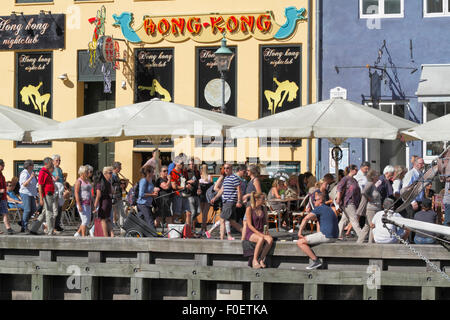 Les gens se rencontrent et parlent d'un verre au soleil dans une ambiance chaleureuse dans le charmant Nyhavn. Beaucoup préfèrent s'asseoir sur le quai parmi les vieux navires. Hygge danois. Banque D'Images