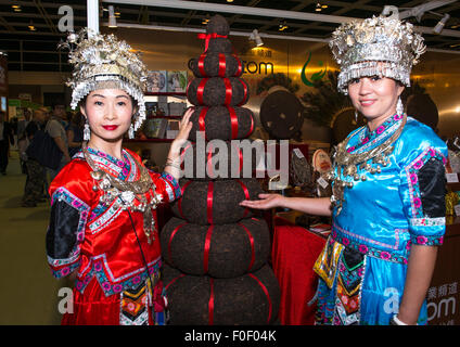 Hong Kong. Août 14, 2015. Dames en robe ethnique traditionnel de l'Wujunong Tea Company en Chine stand by grande tour de briques de thé compressé. Hong Kong's 7th annual Plateau fair au HKCEC réunit le meilleur des mondes à l'un des thés lieu. 12 pays sont représentés à la foire qui est une célébration de la culture et les traditions de plateau et le Hong Kong dispose d'un plateau thé/lait Style Crédit : Jayne Russell/Alamy Live News Banque D'Images