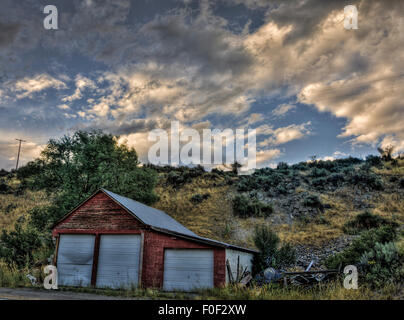 Grange rouge avec portes à l'aube de la lumière. Un ciel partiellement nuageux teinté de couleur rose d'or peut être vu Banque D'Images