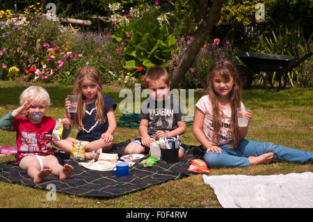 Les enfants ayant un pique-nique dans le jardin sur un jour d'été Banque D'Images