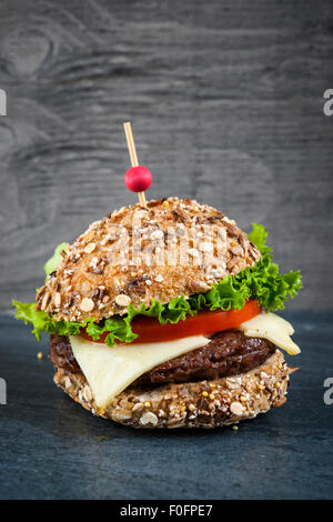 Hamburger gourmet avec fromage suisse et des légumes frais sur pain multigrains sur fond sombre Banque D'Images