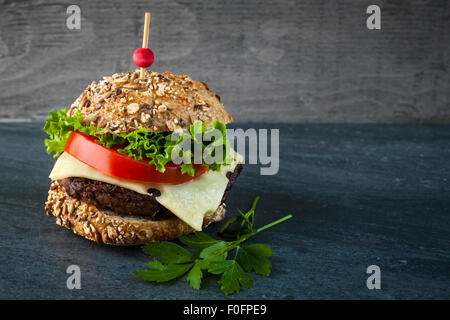 Hamburger gourmet avec fromage suisse, légumes frais sur pain multigrains sur un fond sombre et copy space Banque D'Images
