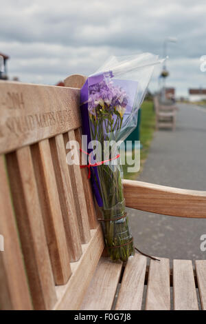 Un bouquet de fleurs laissé sur un banc du souvenir de quelqu'un décédé. Banque D'Images