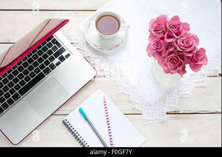 - Le travail à domicile, portable rose roses, verre, blocs-notes et stylos sur un bureau Banque D'Images