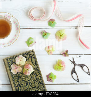 Nature morte au verre d'eau, vieux livre, hortensia, fleurs et ruban ciseaux à broder Banque D'Images