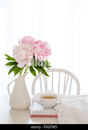 Un bouquet de pivoines rose blanc dans un pot sur la table, avec des magazines, tasse de thé, le tissu et le président dans l'arrière-plan Banque D'Images