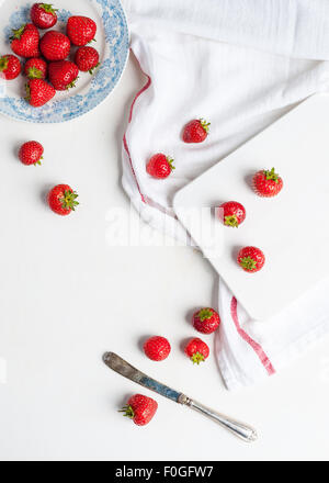 Les fraises dans une assiette blanche et bleue et sur la table et planche à découper Banque D'Images