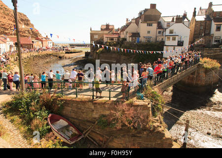 Staithes, UK. Août 15, 2015. La foule en attendant le début de la course de canards annuel recueillir sur le pont au-dessus de Roxby Beck. La RNLI (Royal National Lifeboat Institute) organise chaque année une semaine de collecte de fonds dans le village de pêcheurs de Staithes sur la côte nord-est de l'Angleterre. Dimanche 16 août 2015, UK Crédit : Graham Hardy/Alamy Live News Banque D'Images