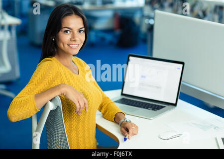 Portrait of a smiling businesswoman sitting occasionnel à la table avec laptop in office Banque D'Images