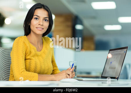 Happy casual businesswoman sitting at the table and looking at camera Banque D'Images