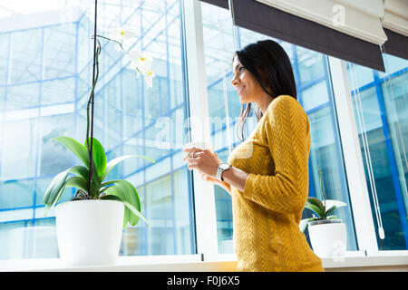 Portrait of a smiling businesswoman holding cup avec café et à at window in office Banque D'Images