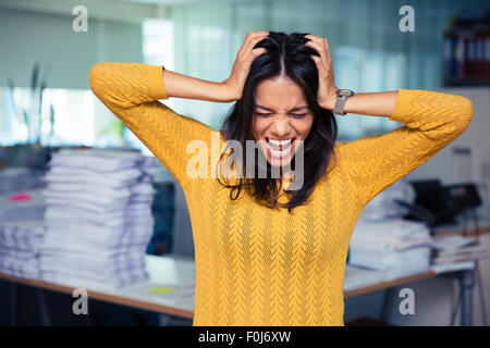 Portrait of a casual businesswoman couvrant ses oreilles et crier in office Banque D'Images