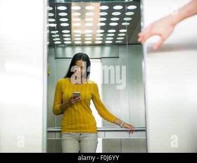 Le portrait d'une businesswoman using smartphone dans l'élévateur Banque D'Images